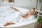 Top view on young blonde attractive female lying in hot bathtub and relaxing in bubbles.