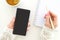 Top view. Young business woman hold smartphone and taking notes in notebook. On table is notepad and cup of tea. On