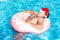 Top view of young drunk guy in santa claus hat swim with pink circle in pool. drunk guy on vacation in the hotel