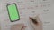 Top view of young entrepreneur girl hands checking green screen smartphone and marking calendar days off with red marker -