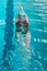 Top view of a young female swimmer training in the pool, swimming on her back underwater. Floats under water and blows