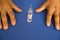 The topic of vaccination of the elderly against coronavirus. An old man`s hands and an ampoule with covid-19 vaccines on the tabl