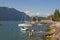 A topless Italian man lying at the edge of small pier enjoying mountain view with yacht boats at Malcesine town, Lake Garda, Italy