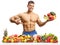 Topless male fitnes model posing with a plate of fruits and vegetables and pointing at his abs