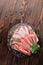 Topview of a plate of thinly sliced prosciutto with fresh green leaves of mint on a wooden brown background.