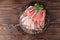 Topview of a plate of thinly sliced prosciutto with fresh green leaves of mint on a wooden brown background.