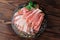 Topview of a plate of thinly sliced prosciutto with fresh green leaves of mint on a wooden brown background.