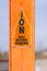 A torn Caution sign on a bright orange post against a blurry background