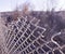 Torn fence of metal mesh covered with frost. Bare trees behind a frozen grid. The concept of freedom behind a frozen metal mesh th