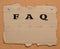 Torn piece of brown cardboard paper is pinned to a corkboard. Inscription FAQ, search for answers to questions, help in