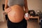 Torso of Pregnant Caucasian female standing, applying cream to her belly. Happy, Active lifestyle in modern home in the