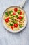 Tortellini with tomatoes and vegetables sauce in white frying pan, close up