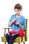 Tortured young girl in a sweater sits on a chair with a red ball of yarn and knitting a scarf and Spitz. Tired. White background.