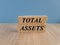 Total assets concept with words on brick blocks. Beautiful wooden table blue background. Capital investment and financial