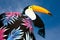 Toucan bird sits on glass edge like cocktail decoration on blue sky background. Vivid vibrant hued colors with copy space. Concept
