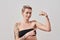 Touch It. Portrait of half naked tattooed woman with short hair looking at camera, pointing at her strong muscle, biceps