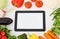 Touch screen digital tablet, fresh vegetables and grass on a white wooden table.