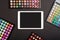 Touchpad with blank screen with colorful eyeshadow palettes on black background. Flat lay