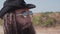 A tough guy with a beard and dark glasses is walking in the desert. Close-up of his face