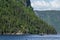 A tour boat is dwarfed by the mountains it is passing by in Saguenay Quebec