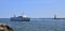 A tour boat full of tourists is seen entering Warnemunde harbor, as it passes a red and white lighthouse and a rock jetty.