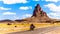 Touring Bike Riders passing the rugged peaks of El Capitan and Agathla Peak towering over the desert landscape of Monument Valley