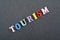 TOURISM word on black board background composed from colorful abc alphabet block wooden letters, copy space for ad text