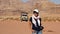 Tourist Asian woman carrying camera in Wadi Rum desert, Jordan with safari car behind.