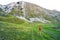 A tourist with a backpack and hiking sticks walking through a green valley at the foot of a beautiful mountain.