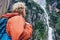 Tourist with backpack looks on forest waterfall in rainy mountain