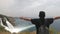 Tourist with a backpack, standing arms outstretched in different directions near the beautiful waterfalls on a steep