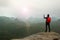 Tourist with backpack takes photos with smart phone of rainy vally. Dreamy foggy valley below