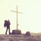 Tourist with big backpack stand at cross memorial on mountain peak. Man is watching into misty Alpine valley bellow. Metal cross.