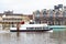 Tourist boat cruising along the River Thames passing the Riverside Walk promenade in Kingston upon Thames, England