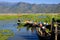 Tourist boats arrive at peer on floating farm. Mountain scenery background