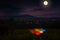 Tourist camping near forest in the night. Illuminated tent under beautiful night sky full of stars and full moon. Hiking in
