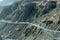 A tourist car far distant away on long mountain hill road trip. Driving at the edge of Desert Himalayas. Dust trails of vehicle