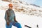 A tourist in a down jacket and sunglasses with gloves stands in the mountains of the Caucasus next to the skis and