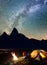 Tourist family sitting face to face in front tent near campfire under shines starry sky at night. Long exposure