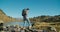 Tourist female crossing mountain river flowing into lake with hike backpack