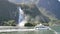 Tourist ferry carrying people and waterfall at Milford Sound in South Island of New Zealand