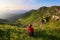 The tourist girl with back sack and tracking sticks sits on the lawn. Relaxation. Mountain landscapes. Wonderful summer day.