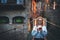 Tourist girl blonde with glasses and camera stands on suspension bridge of old historical city uses smartphone to plan walk