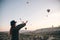 A tourist girl in a hat admires hot air balloons flying in the sky over Cappadocia in Turkey. Impressive sight.