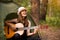 Tourist girl in hat sits in tent and playing guitar concept. Tourism rest on nature.