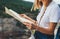 Tourist girl holding in hands map resting during summer vacation on background green mountains landscape, traveler woman plans