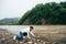 Tourist girl in jeans and white sweatshirt touching the yellow water on the bank of the dirty mountain river surrounded