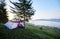 Tourist girl sitting alone in the entrance of tourist tent on grassy green hill under pine tree