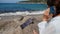 A tourist girl is talking on a smartphone on the seashore. The phone is charged by a solar panel that lies on a stone.