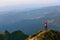 The tourist girl with the tracking sticks and the back sack at the edge of the cliff. The landscape with the high mountains.